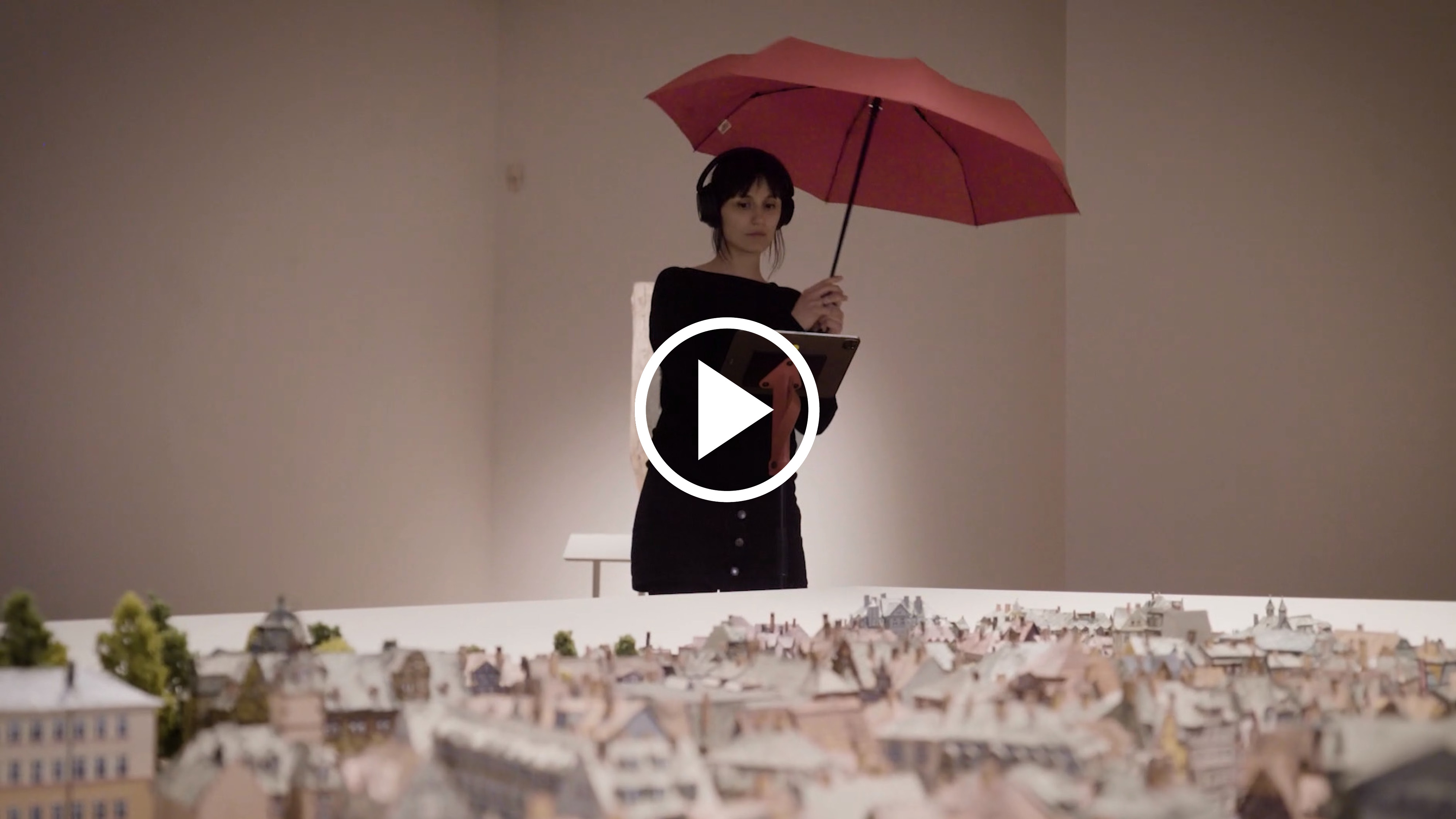 Eine junge Frau steht mit einem I-Pad und einem Regenschirm vor einem durch Augmented Reality erweiterten Stadtmodell